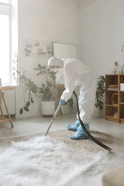 A woman performing surface cleaning in a living room, vacuuming a patterned area rug with floral motifs and muted colors. She is standing on a wooden floor adjacent to the rug, wearing casual clothing